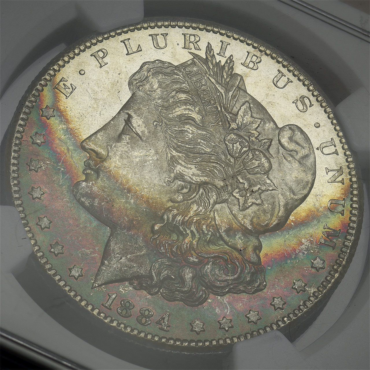 Gallery image of this 1884-CC Morgan Dollar NGC MS-63 Eye Candy – Series 1 Bullion Plus Label, Dark Banded Rainbow Crescent Toning